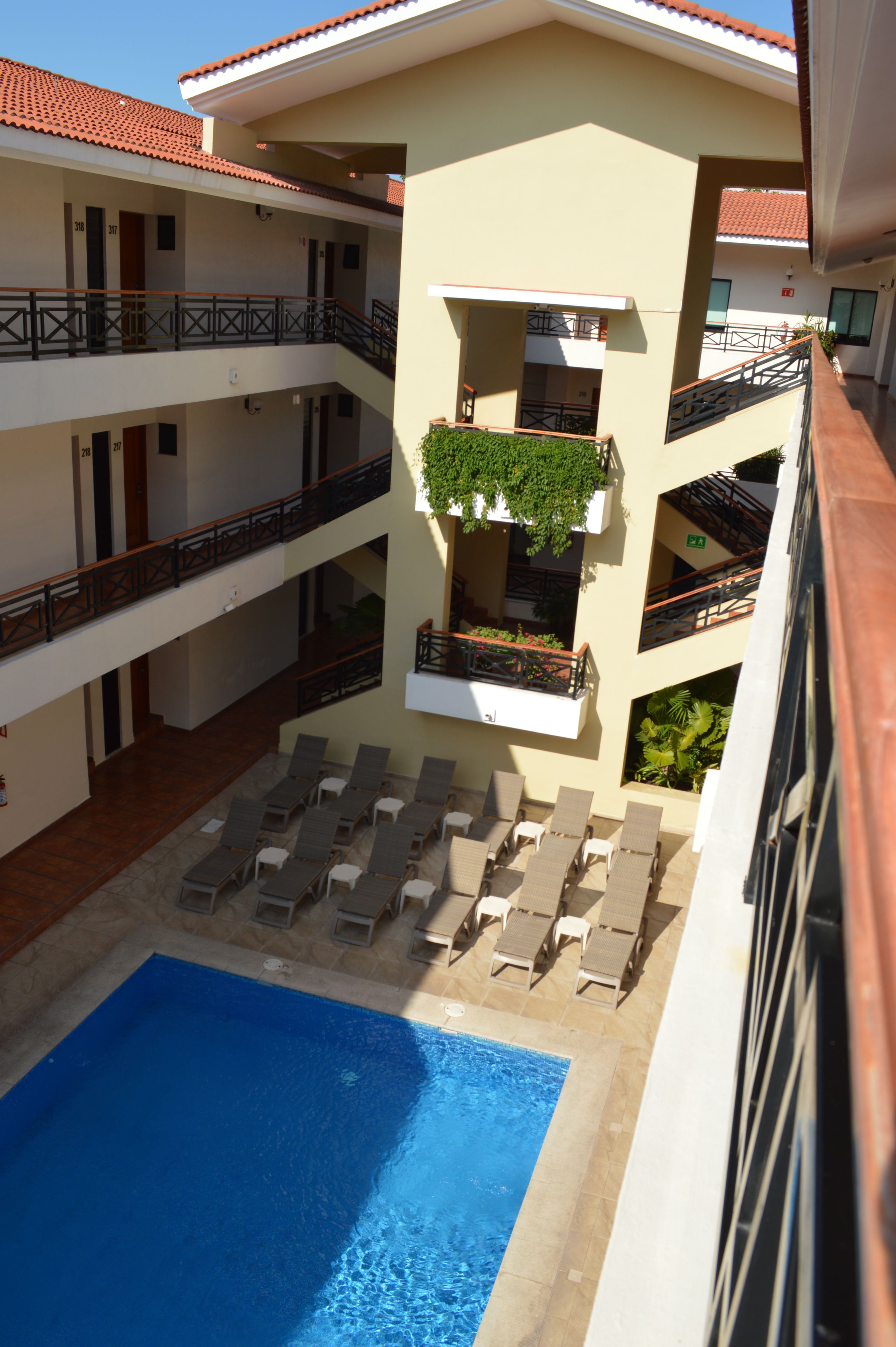A hotel with a swimming pool, multiple balconies, and lounge chairs.