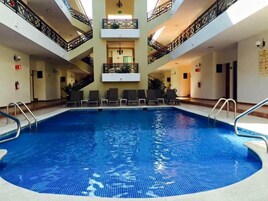 Una piscina interior de varios niveles con agua cristalina, rodeada de sillones de descanso y barandillas.