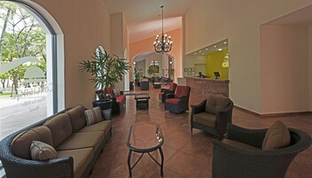 Un vestíbulo amplio con mobiliario de mimbre, una mesa de recepción y una planta grande en maceta.