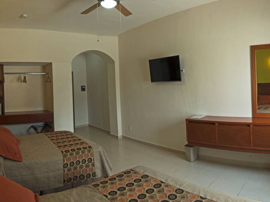 Habitación de hotel con dos camas, un escritorio, un televisor, un espejo y un ventilador de techo.