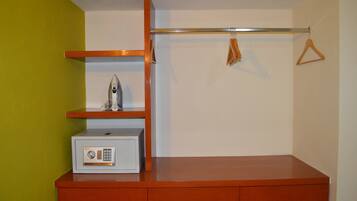 A compact room with a wooden desk, a small safe, and a coat rack with hangers.