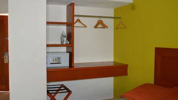 Un dormitorio compacto con escritorio integrado, perchero y cama con manta naranja.