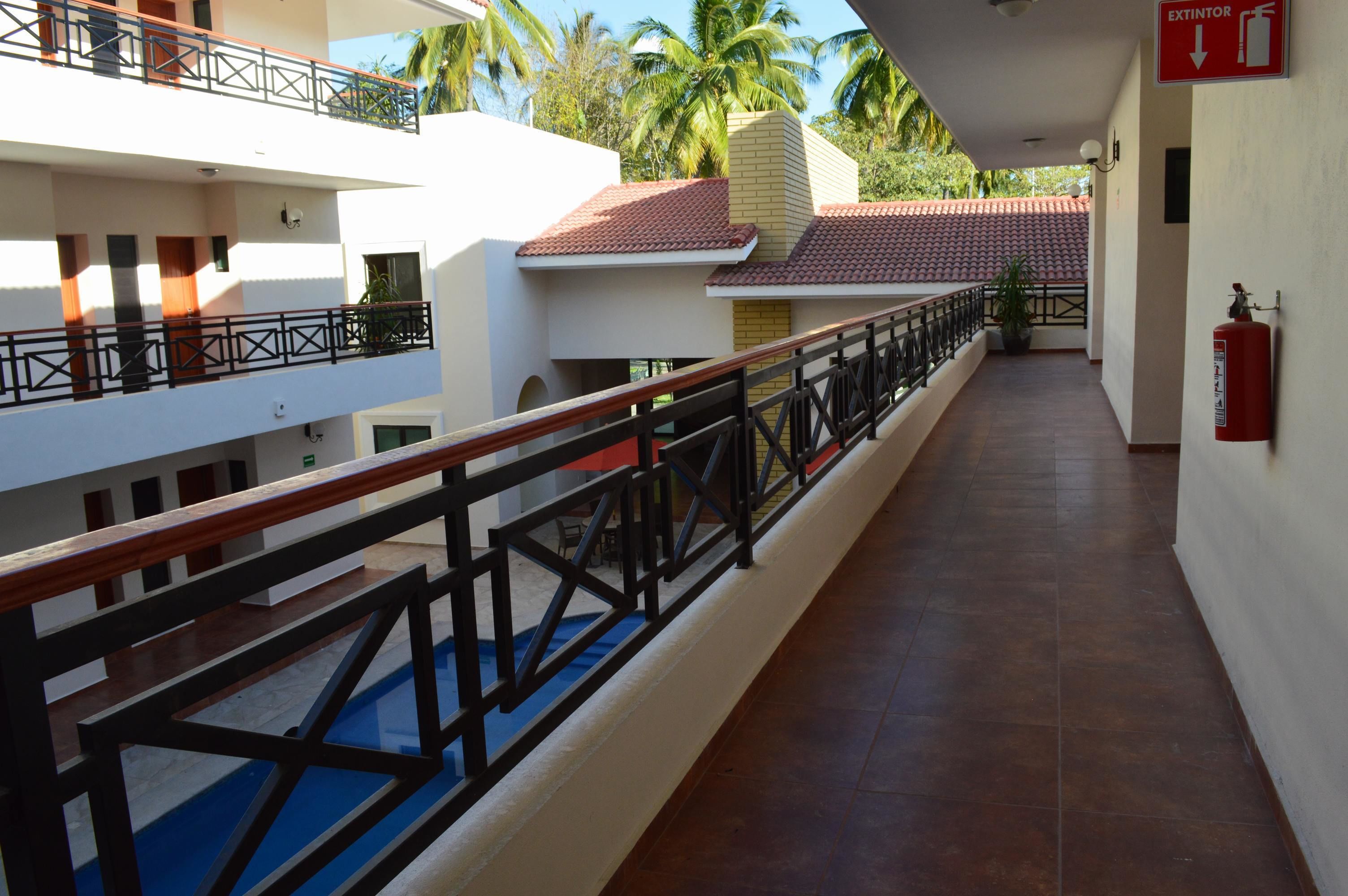 A corridor with a tiled floor, a wooden railing, and a fire extinguisher on the wall.