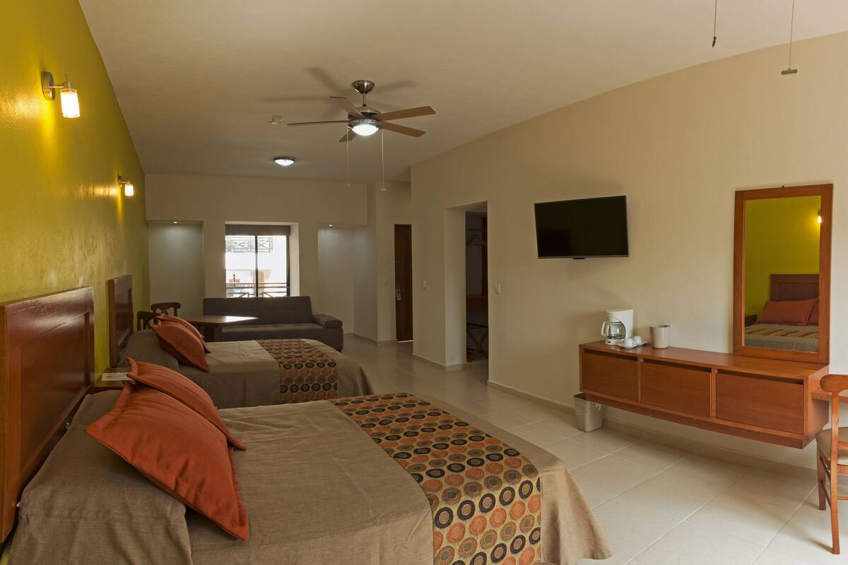 Habitación de hotel con dos camas, un escritorio, una silla, un televisor y un ventilador de techo.