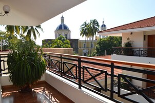 Un balcón con suelo de baldosas, una planta en maceta y vista a un edificio de arquitectura abovedada.