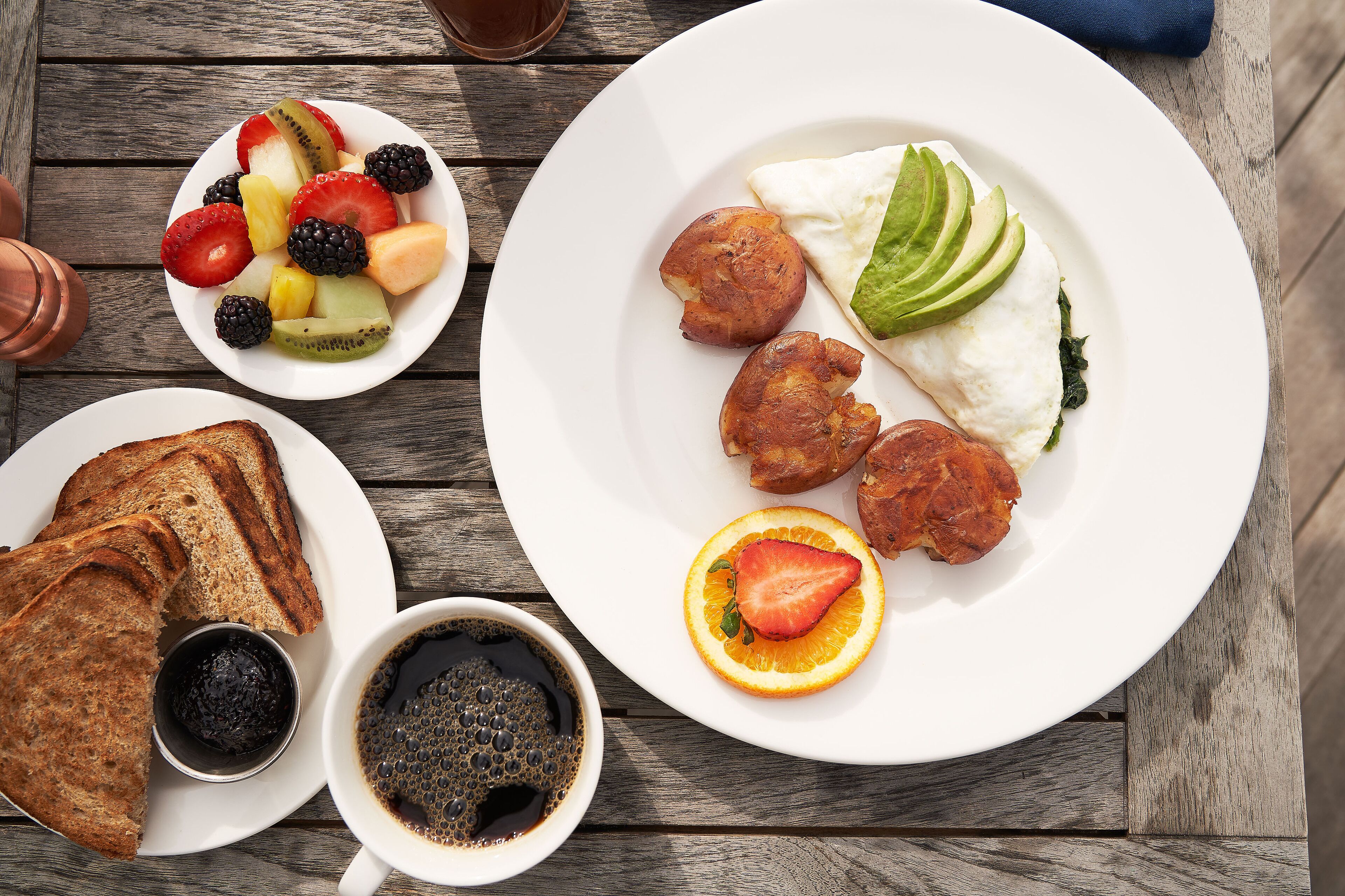 A breakfast setting with toast, fruit, eggs, and coffee on a wooden table.
