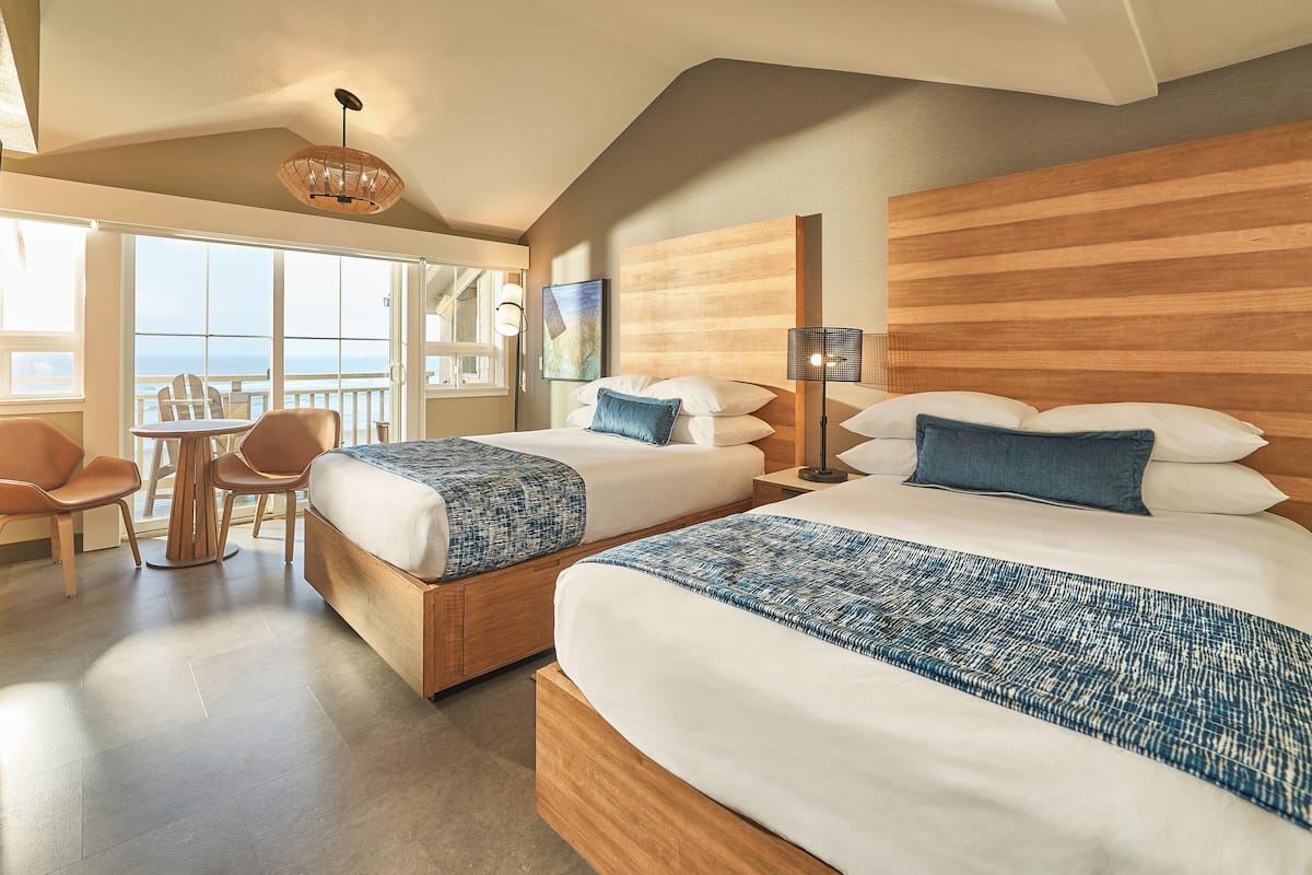 A hotel room with two beds, a balcony, a dining area, and a view of the sea.