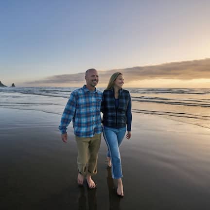 A couple walking on a beach with a sunset in the background.