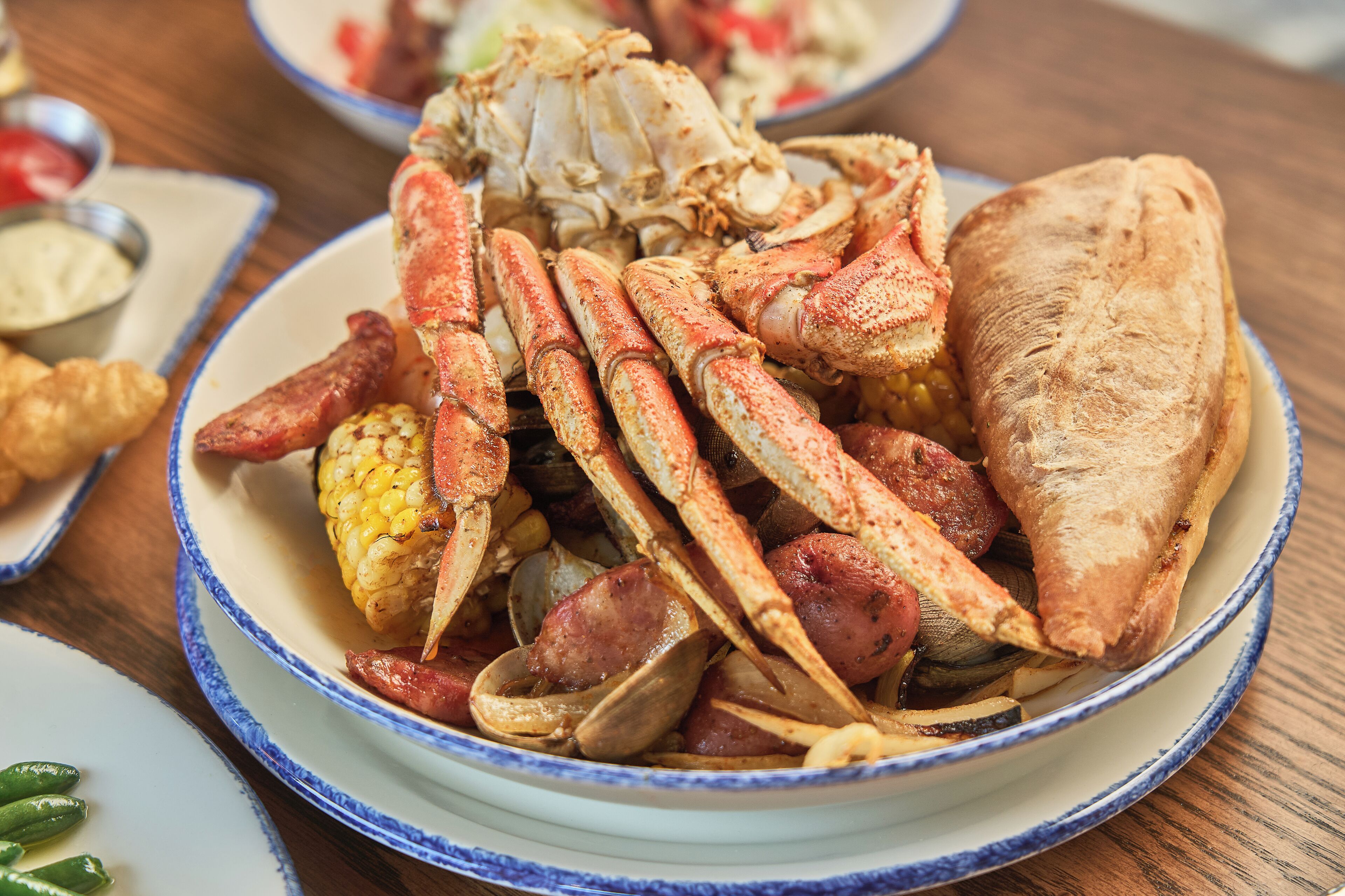 Un plato de mariscos con patas de cangrejo, salchicha, maíz y almejas.