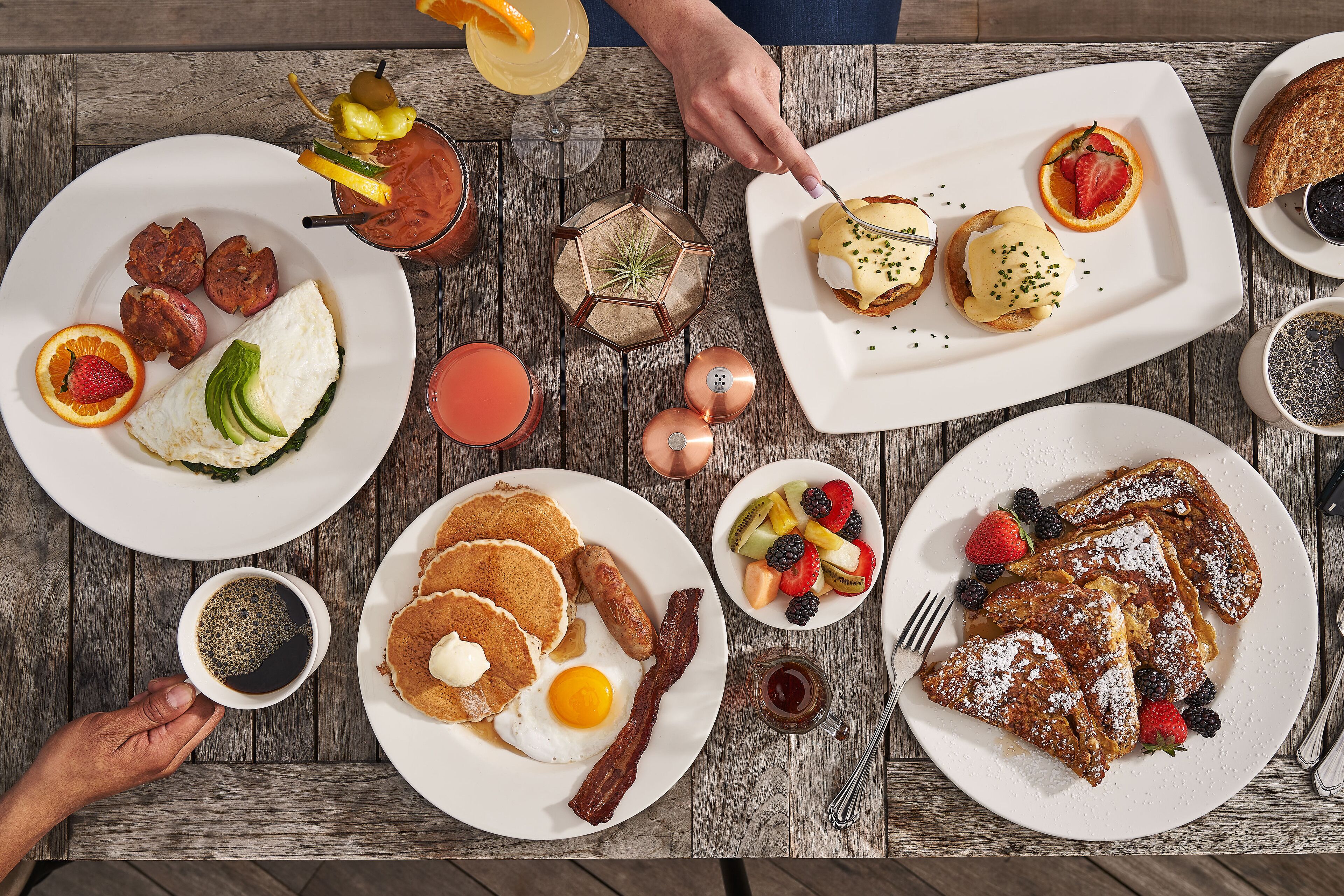 Ein Frühstückstisch mit verschiedenen Speisen, darunter Pfannkuchen, Eier, Speck und Obst.