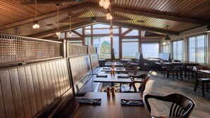 Un restaurante con interior de madera, mesas, sillas y amplios ventanales con vista al océano.