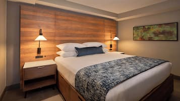 Ein Hotelzimmer mit einem hölzernen Kopfteil, zwei Nachttischlampen, einem Bett mit weißen Bettwäsche und einer gemusterten Tagesdecke, einem Nachttisch und einem Bild an der Wand.