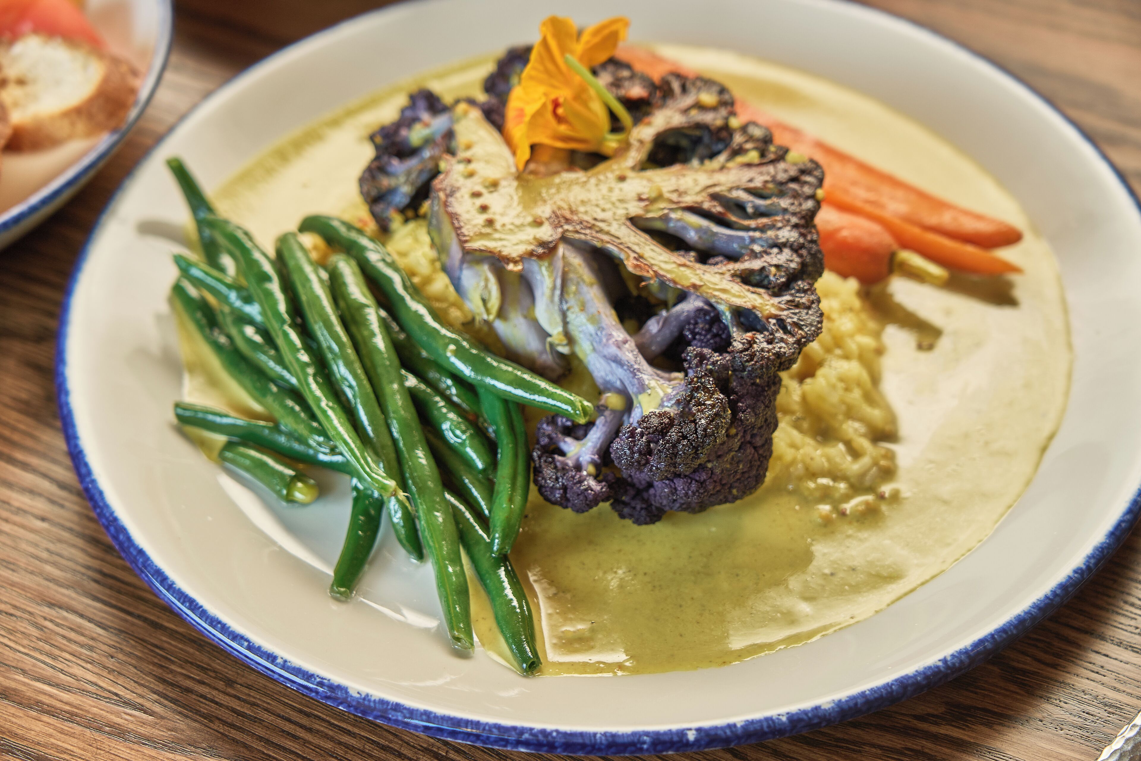 A plate with roasted cauliflower, green beans, and carrots on a white plate with a blue rim.