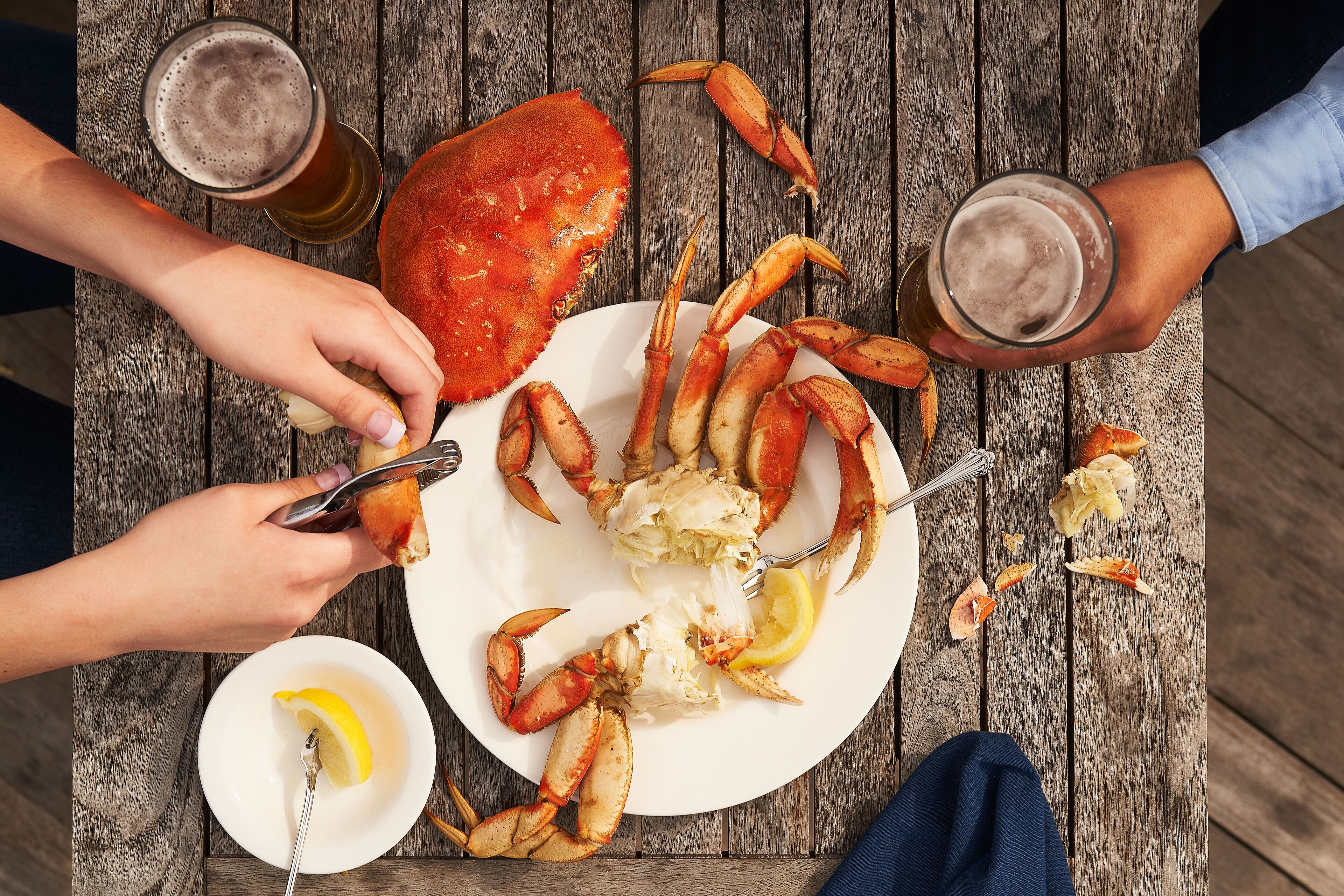 A wooden table with a plate of crab, a glass of beer, and a lemon wedge.