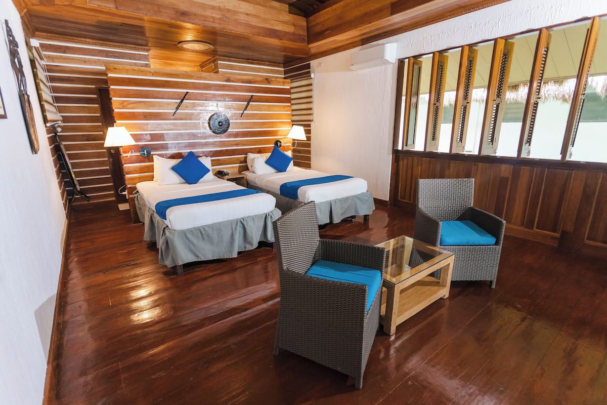 Une chambre avec deux lits, des chaises en osier et un plancher en bois.