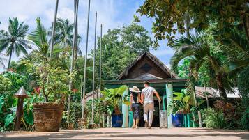 A couple walking towards a traditional thatched-roof building surrounded by lush tropical vegetation.
