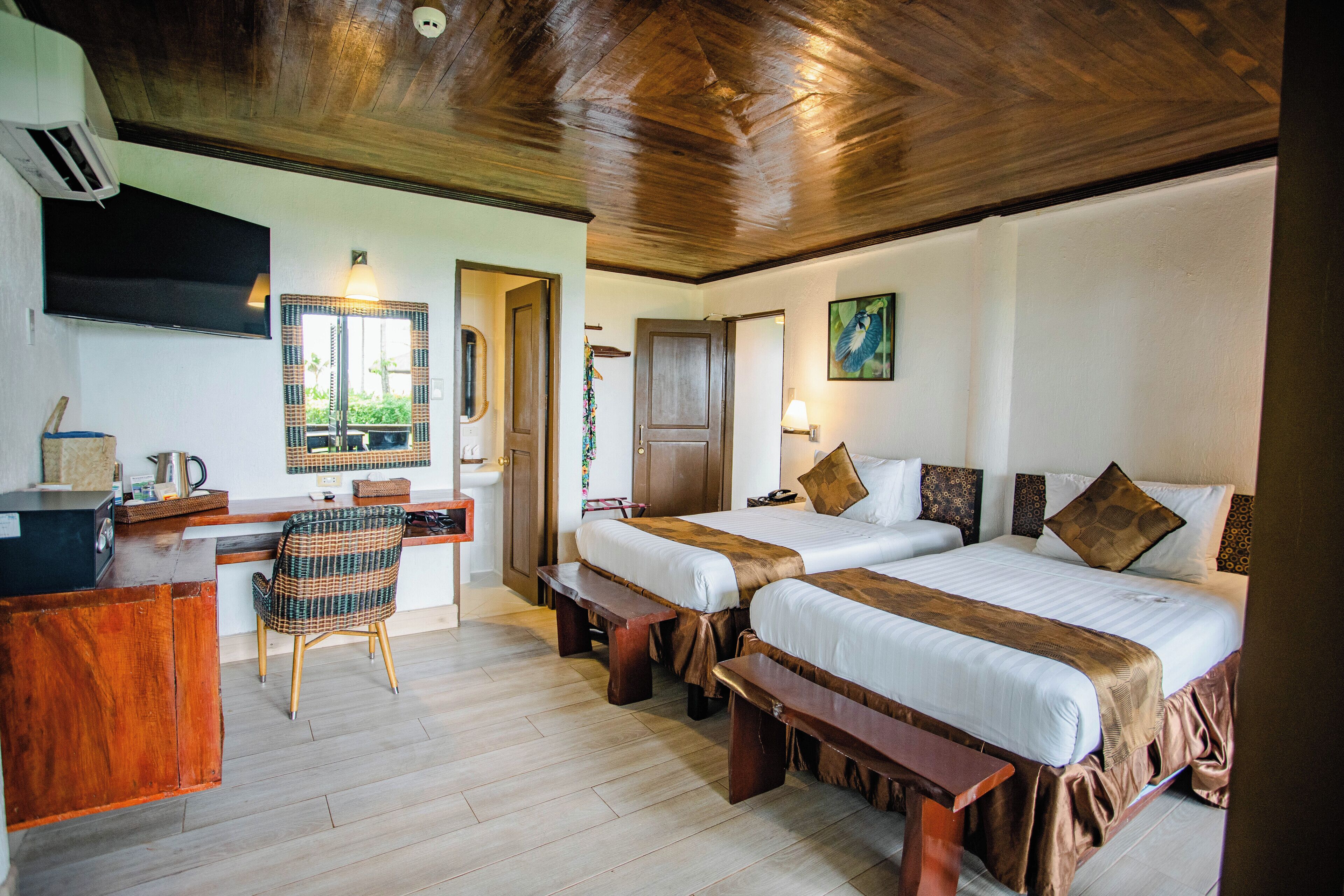 Una habitación de hotel con dos camas, un escritorio de madera, una silla y un banco.