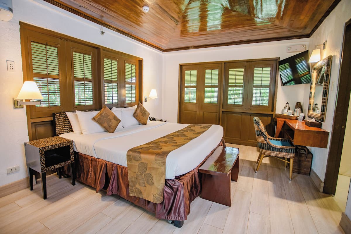 Une chambre d’hôtel avec un grand lit, un bureau en bois, une chaise et un téléviseur fixé au mur.