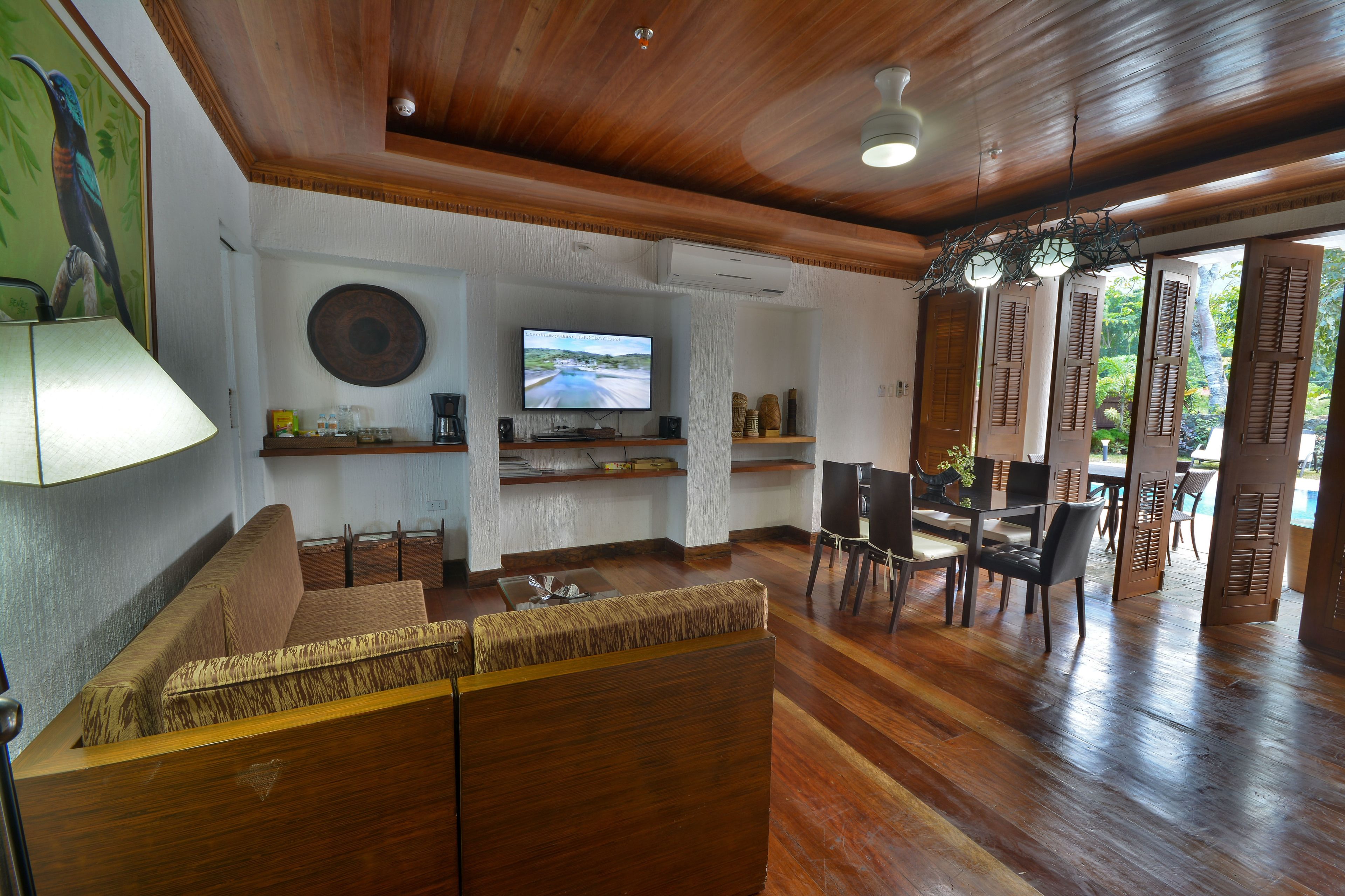 A spacious living area with a wooden ceiling, a television, a sofa, and a dining table with chairs.