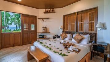 Habitación de hotel con una cama grande, contraventanas de madera, vistas a palmeras y un banco de madera.