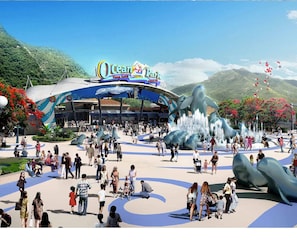 Un espacio exterior concurrido con un gran letrero de Ocean Park, que presenta una escultura de delfín y fuentes de agua.