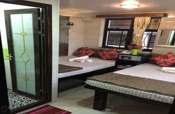 Habitación de hotel pequeña con cama, una mesita, un banco, una mesita de noche con lámpara y una ventana con cortinas.