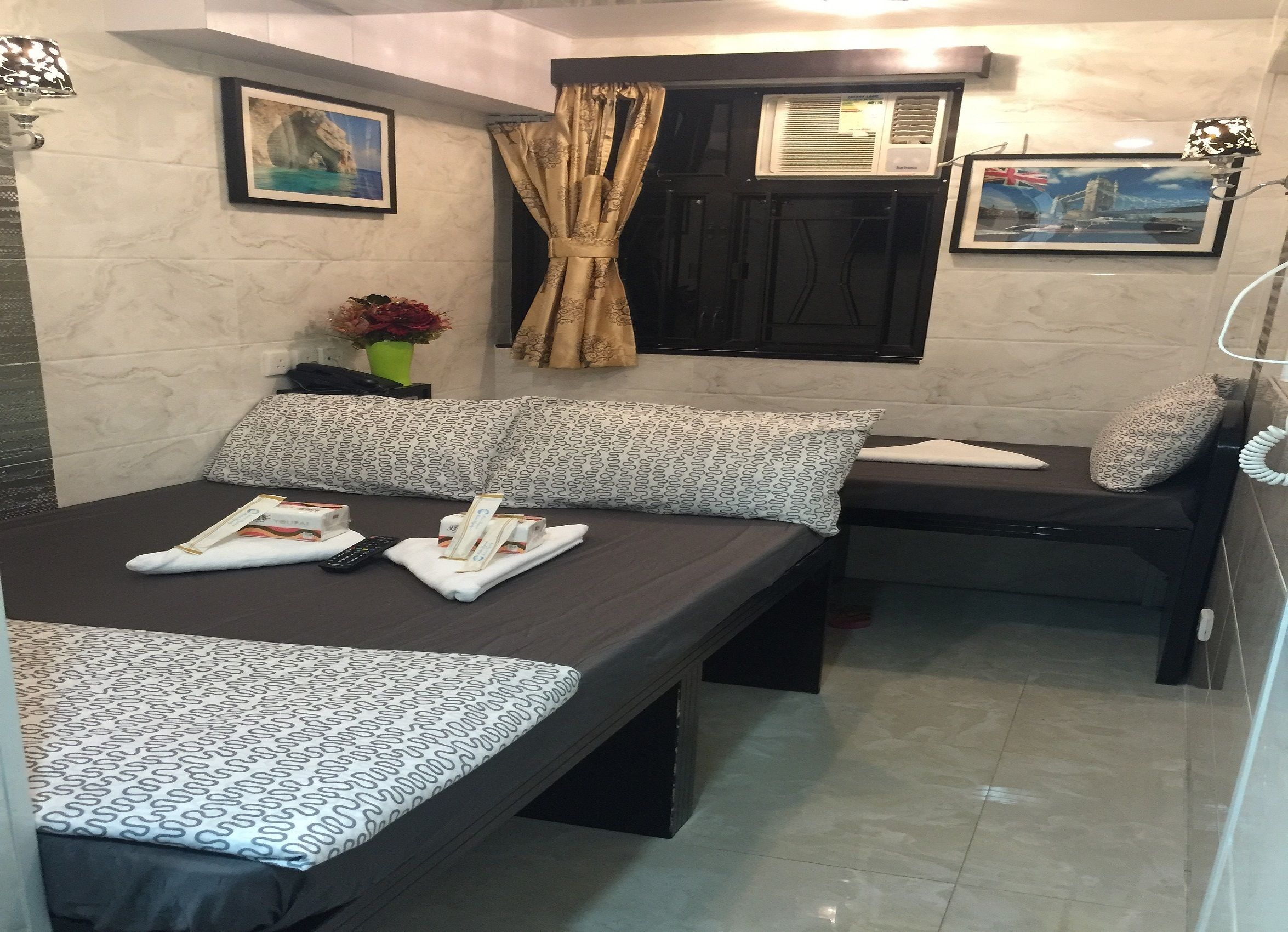 Habitación de hotel con cama, un banco y una mesita. Sobre la cama hay toallas y un control remoto.
