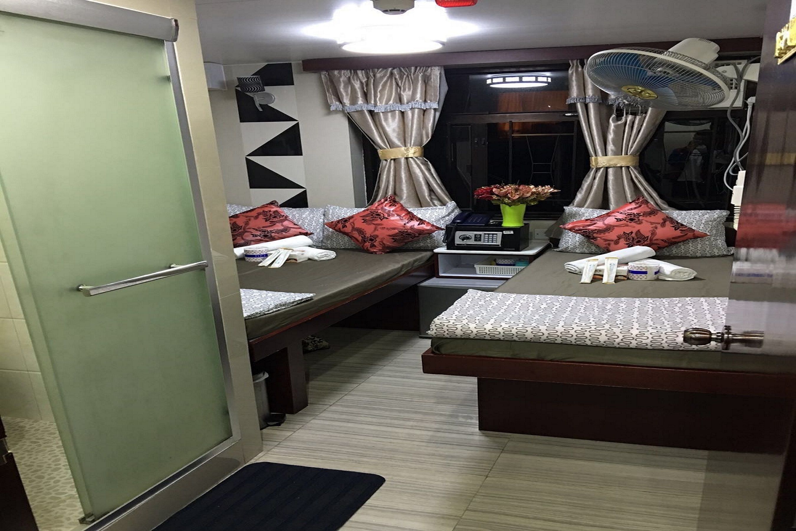 A compact room with a bed, bedside tables, a fan, and a curtain.