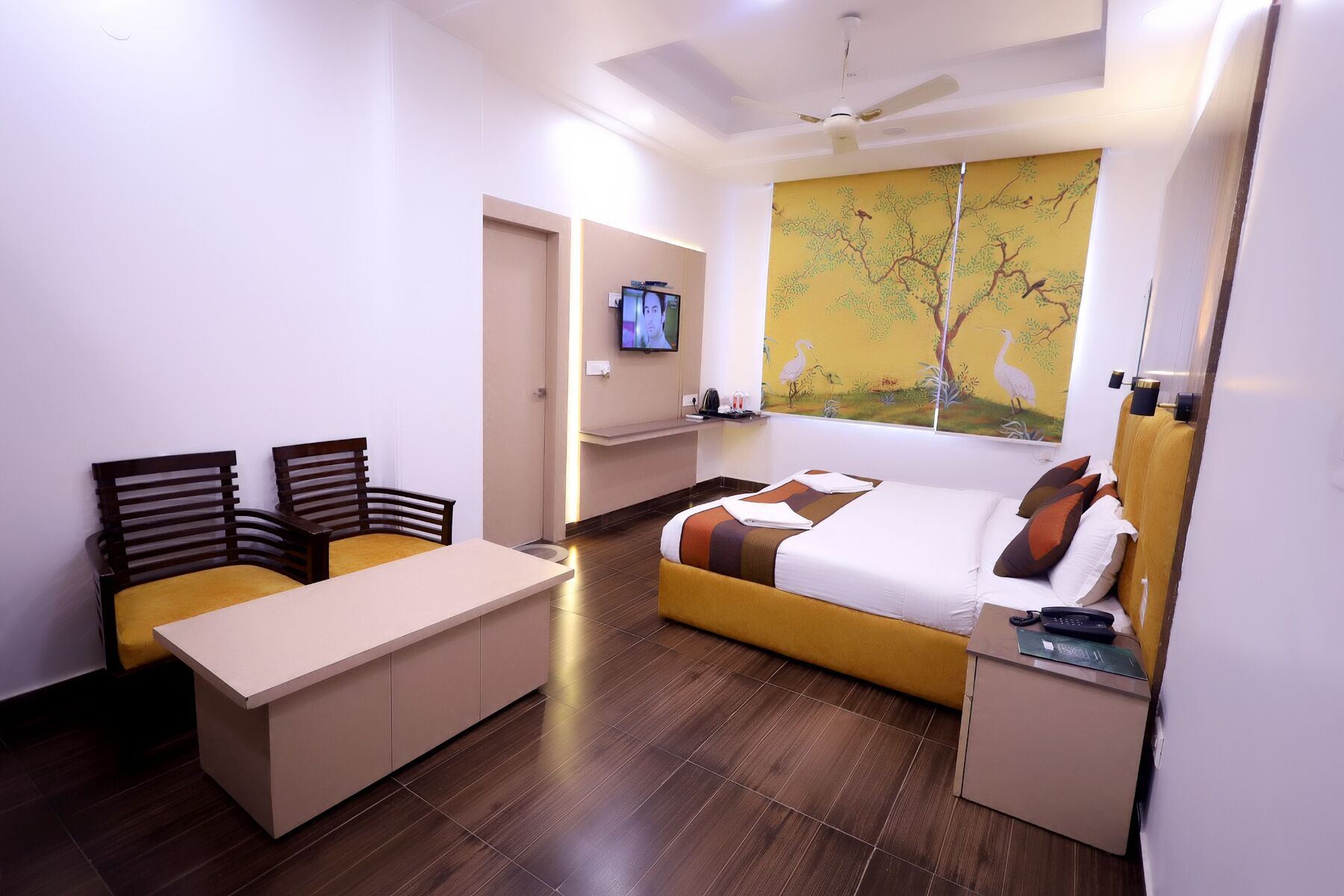 A modern hotel room with a bed, a desk, two chairs, a television, and a painting on the wall.
