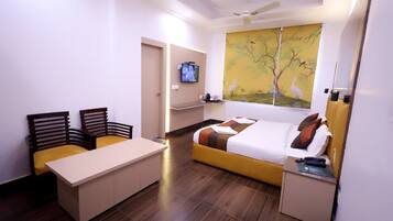 A modern hotel room with a bed, a desk, two chairs, a television, and a painting on the wall.