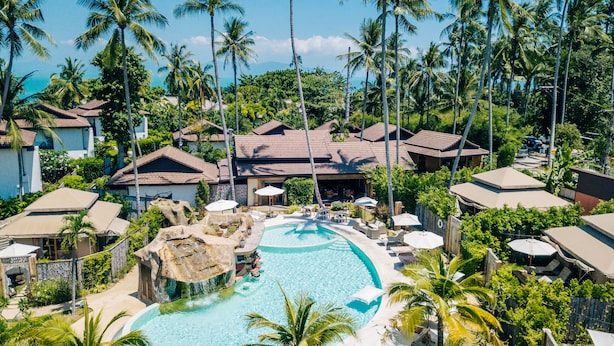 Un complexe hôtelier doté d’une piscine entourée de palmiers et offrant une vue sur l’océan.
