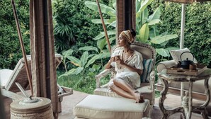 Une personne est assise sur un fauteuil rembourré dans une pièce au décor rustique, entourée de verdure.