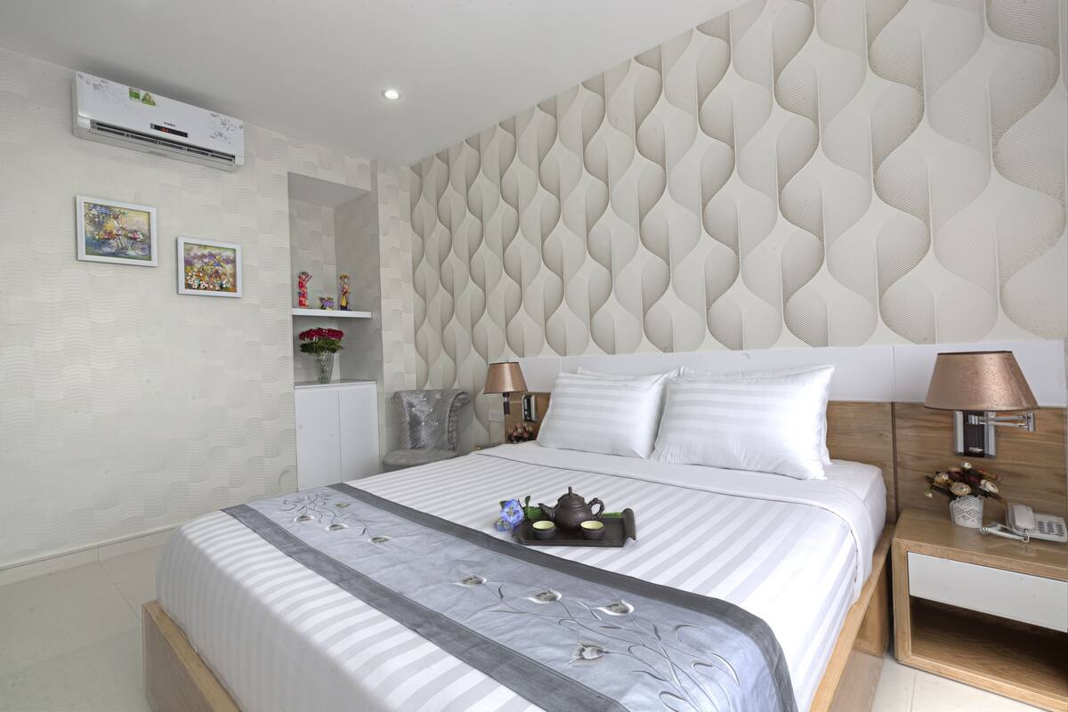 Ein ordentlich eingerichtetes Hotelzimmer mit einem großen Bett, Nachttischen, einer Wand-Klimaanlage und dekorativen Kissen.