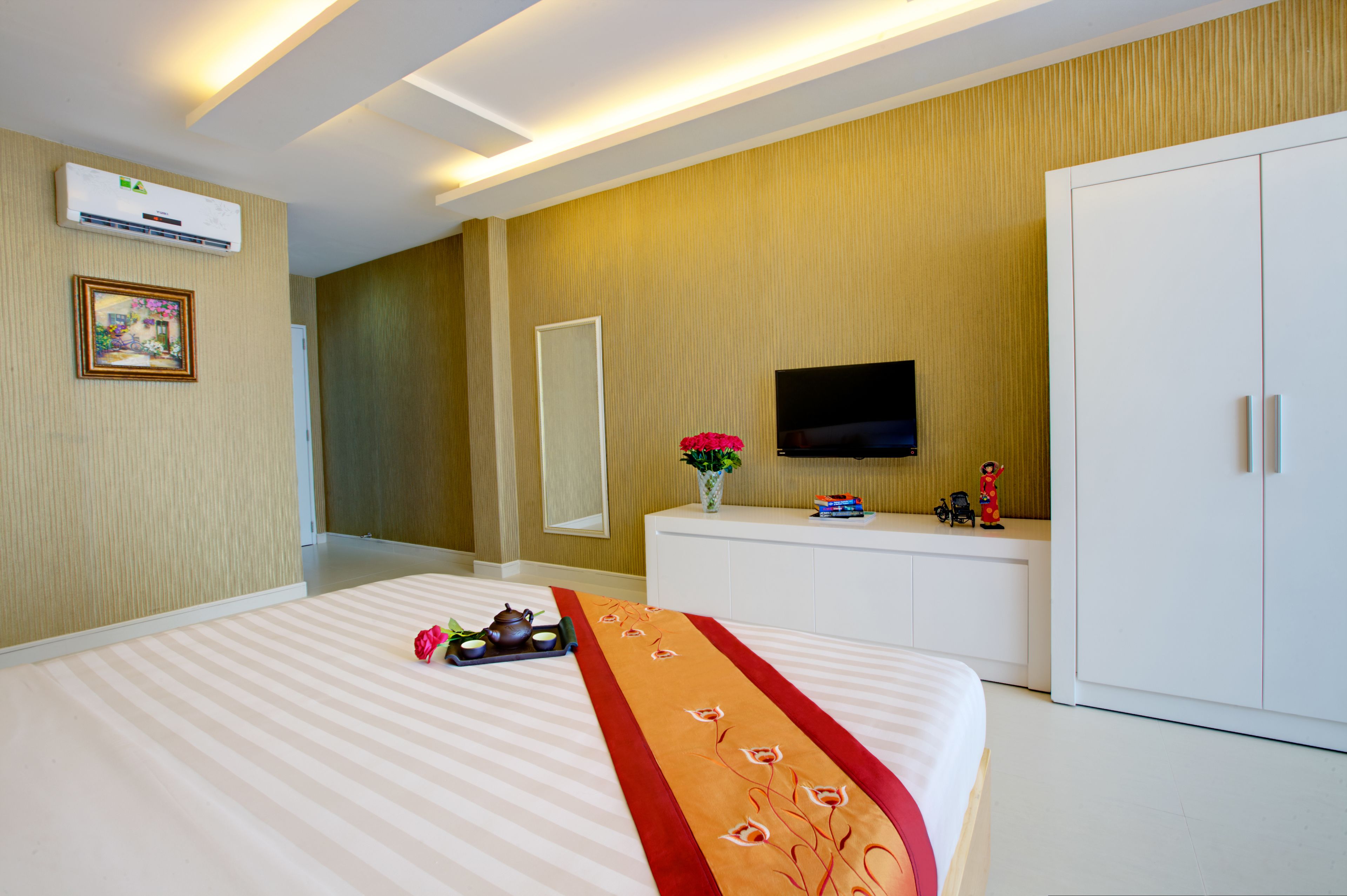 Ein Hotelzimmer mit einem großen Bett, einem Fernseher auf einem weißen Schrank, einem Spiegel und einer Wandklimaanlage.