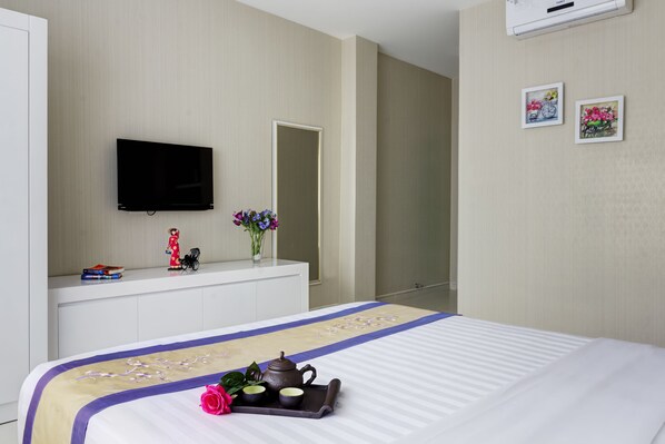 A hotel room with a bed, a flat-screen TV mounted on the wall, a dresser with decorative items, and a mirror.