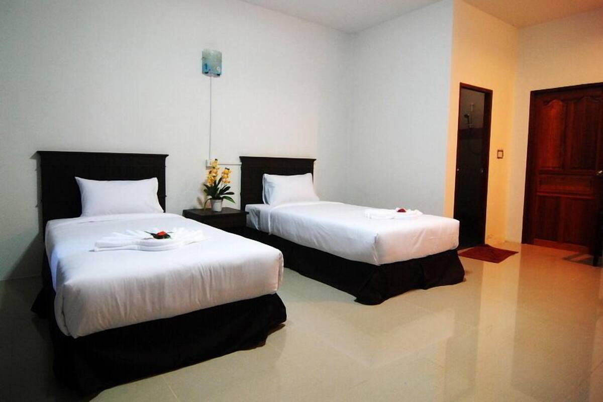Una habitación de hotel con dos camas individuales, una mesita de noche con un jarrón de flores y una puerta de madera.