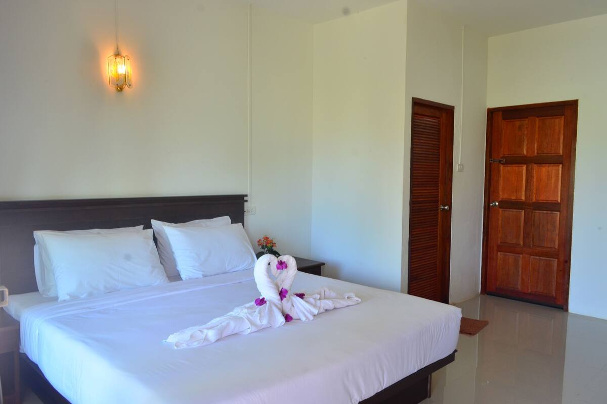 Habitación de hotel con una cama bien hecha, una puerta de madera y una lámpara fijada a la pared.