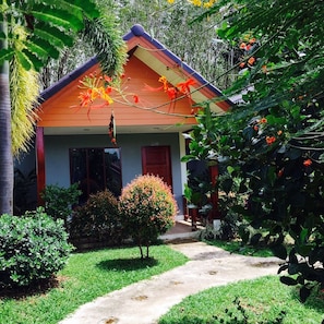 A house with a red roof, a small porch, and a well-maintained garden with various plants and flowers.
