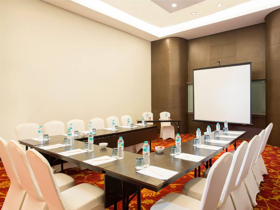 A conference room with a long table, white chairs, water bottles, and a projector screen.