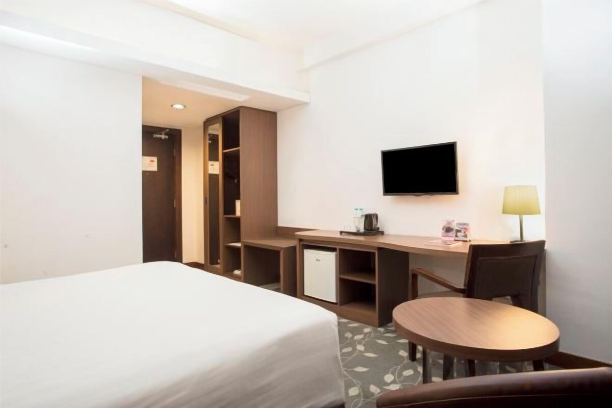 Quarto de hotel com cama, escrivaninha, televisão e uma mesinha.