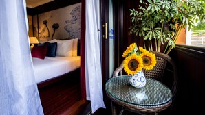 Una habitación con cama, una mesa de vidrio con un jarrón de girasoles y una silla de mimbre.
