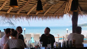 Un bar en la playa con techo de paja, con vista al océano.