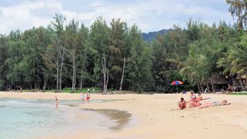 A beach with people sunbathing and swimming, surrounded by trees and a clear sky.