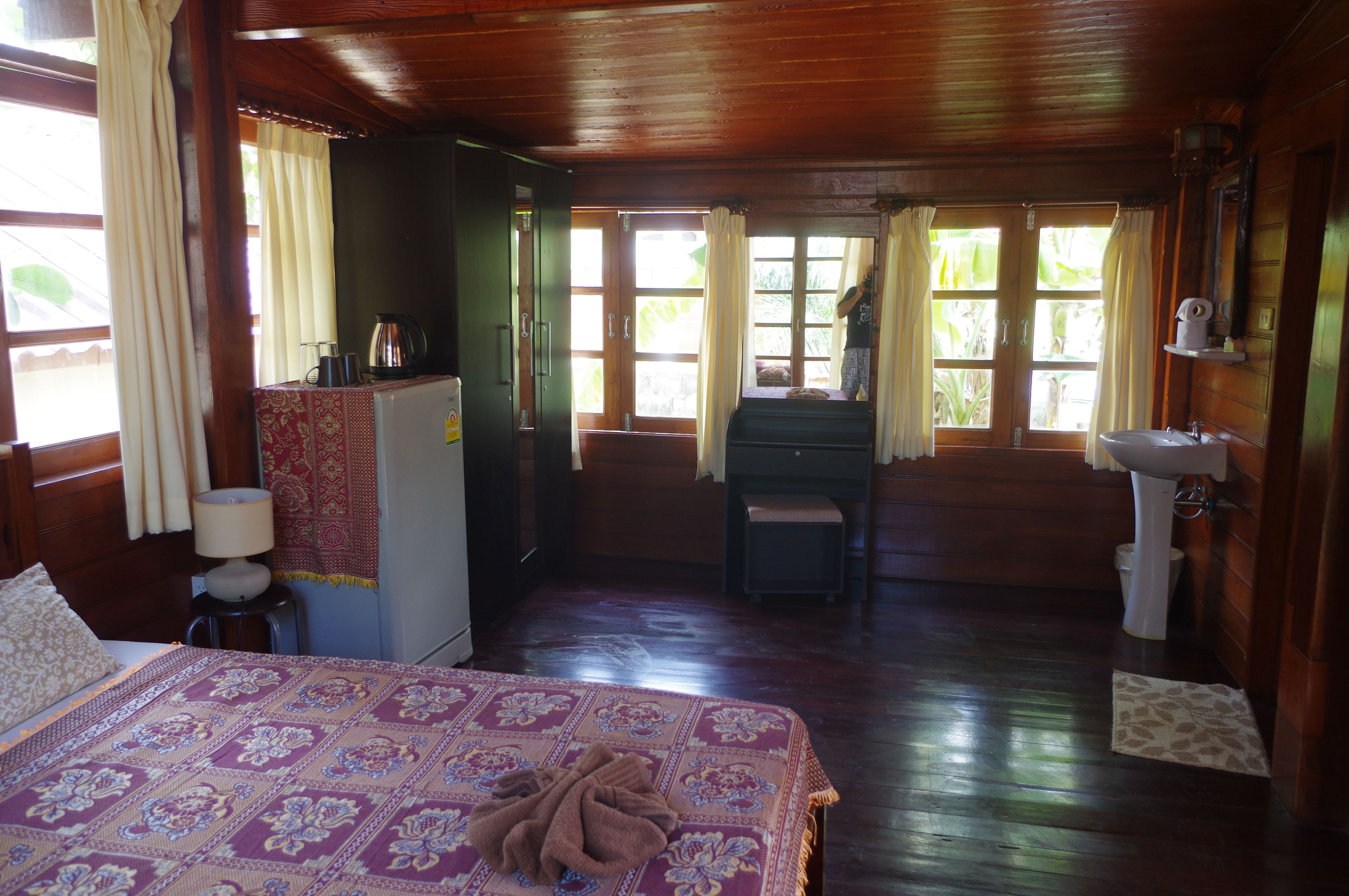 Quarto de cabana de madeira com uma cama, uma escrivaninha, uma cadeira, uma pia e uma janela com cortinas.