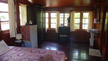 Quarto de cabana de madeira com uma cama, uma escrivaninha, uma cadeira, uma pia e uma janela com cortinas.