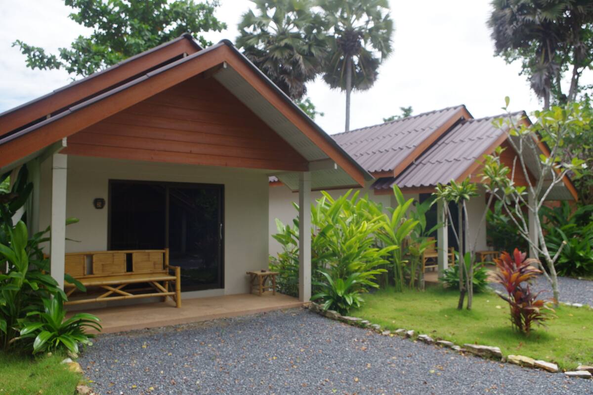A small, single-story building with a sloped roof, a wooden bench outside, and a gravel driveway.