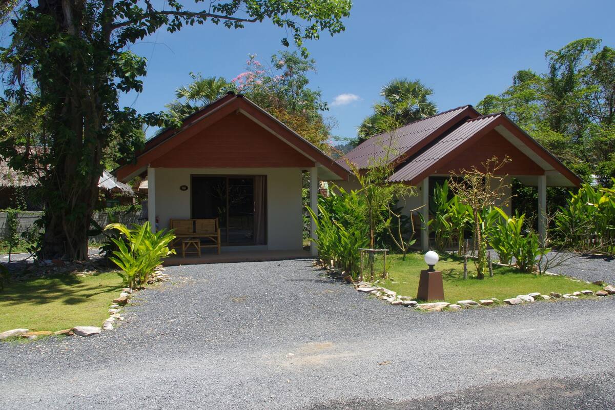 A two-story building with a red roof and a covered porch. There is a gravel driveway leading to the entrance.