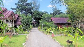 A pathway leading to a row of rustic-style buildings with red roofs, surrounded by lush greenery and trees.