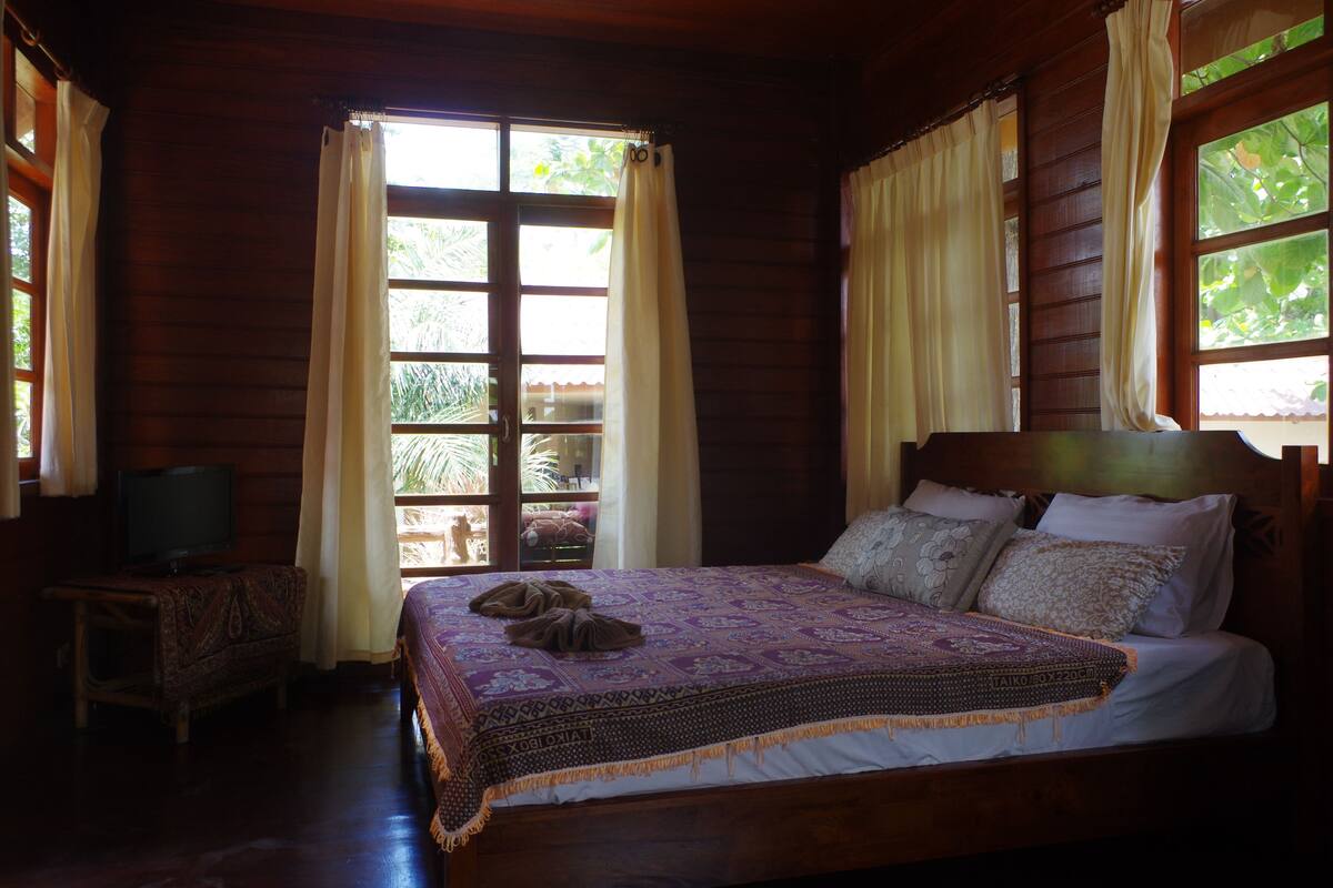 A wooden room with a bed, curtains, a television, and a window.