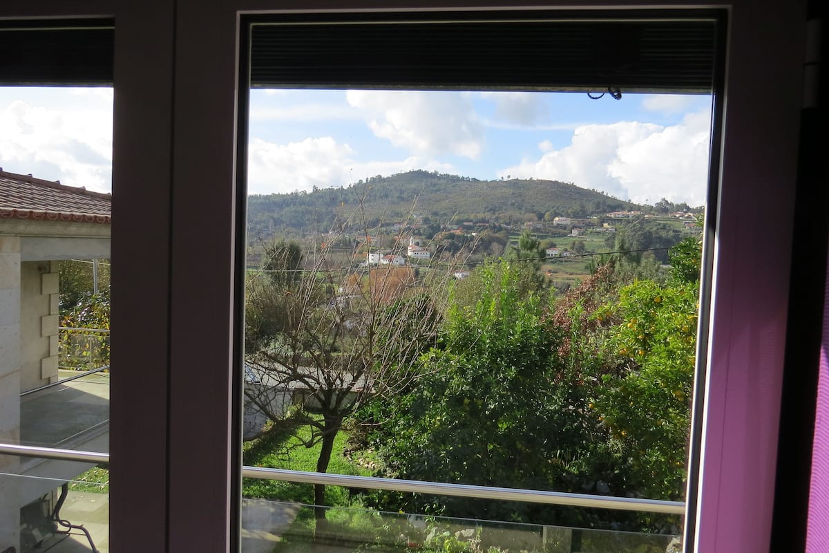 Une vue depuis une fenêtre donnant sur une colline, avec des bâtiments et de la végétation.